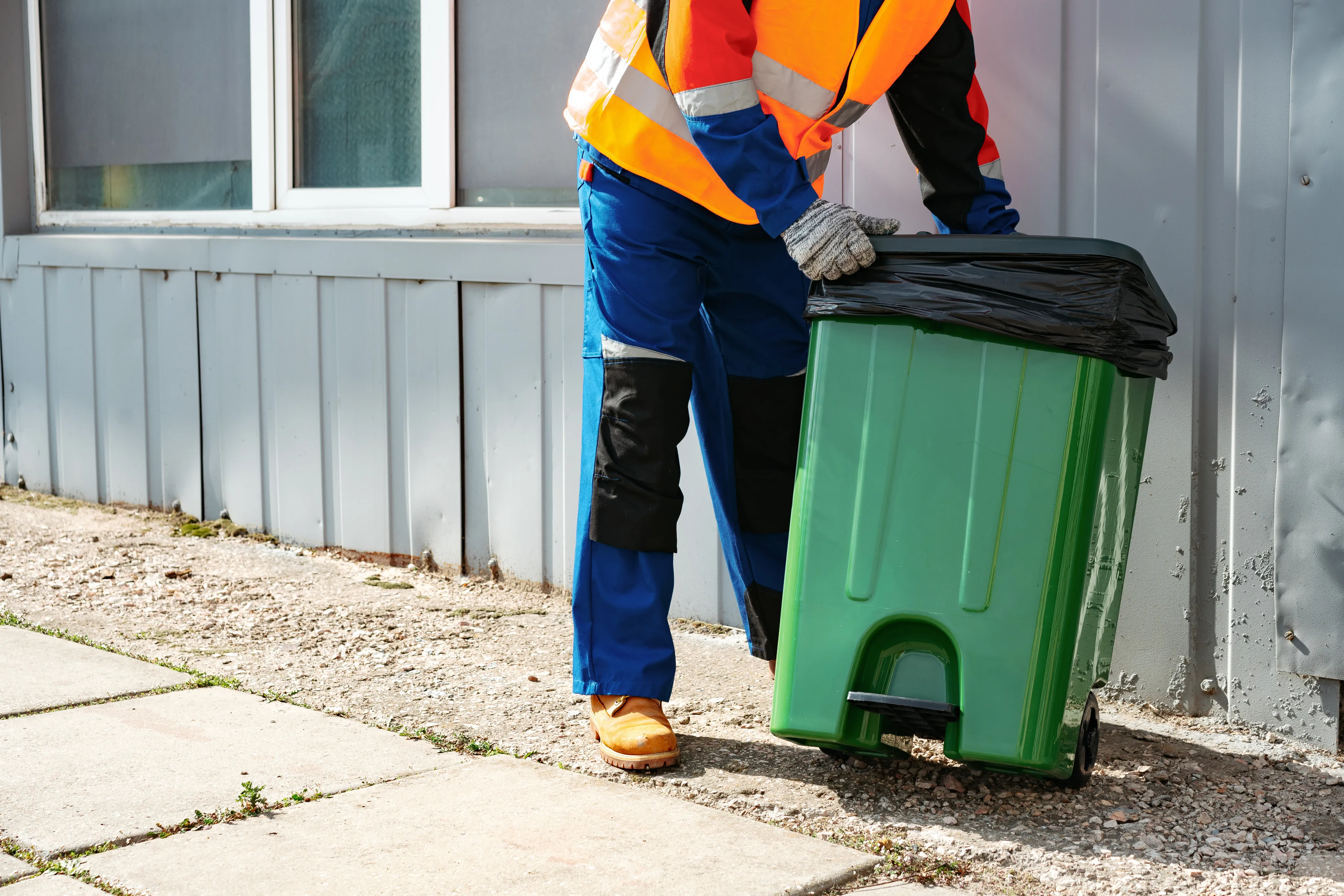 Worker cleaning a green trash bin
